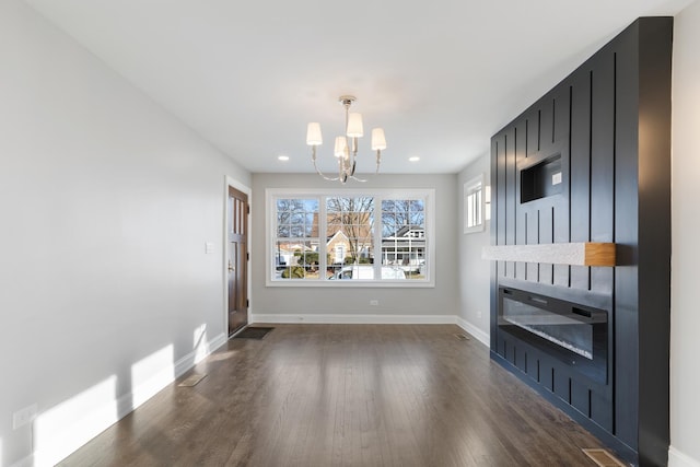 unfurnished living room with dark hardwood / wood-style flooring, a large fireplace, and an inviting chandelier