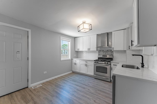 kitchen with white cabinetry, sink, wall chimney range hood, stainless steel range with gas cooktop, and light wood-type flooring