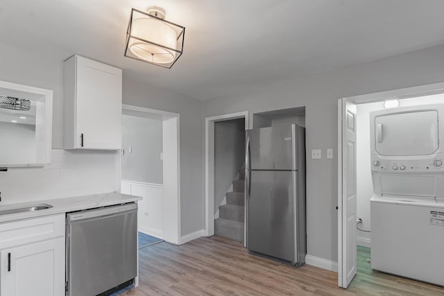 kitchen featuring white cabinets, light hardwood / wood-style floors, stainless steel appliances, and stacked washer and clothes dryer