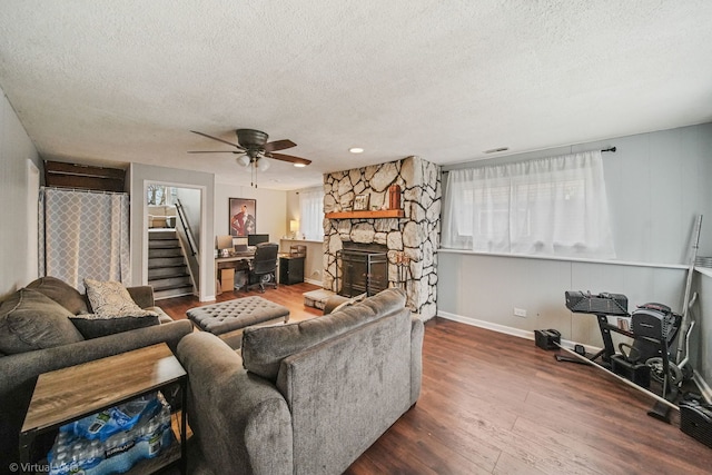 living room featuring a textured ceiling, dark hardwood / wood-style flooring, a stone fireplace, and ceiling fan