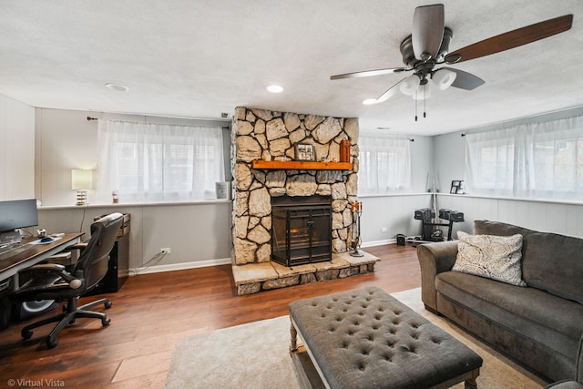 home office featuring a textured ceiling, dark hardwood / wood-style flooring, a stone fireplace, and ceiling fan