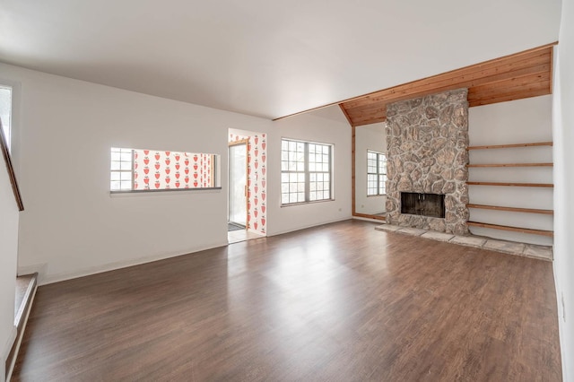 unfurnished living room featuring lofted ceiling with beams, dark hardwood / wood-style flooring, and a stone fireplace