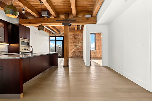 kitchen featuring dark brown cabinets, stainless steel microwave, sink, brick wall, and beamed ceiling