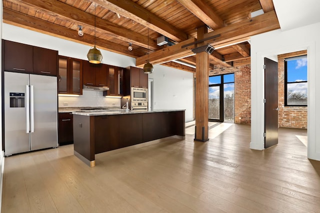 kitchen with a kitchen island with sink, brick wall, decorative backsplash, beamed ceiling, and stainless steel appliances