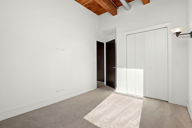 unfurnished bedroom with wooden ceiling, a closet, high vaulted ceiling, light colored carpet, and beam ceiling