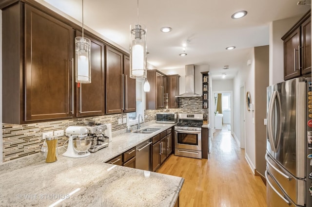 kitchen with pendant lighting, sink, wall chimney exhaust hood, light stone countertops, and appliances with stainless steel finishes