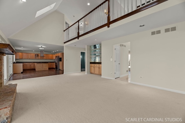 unfurnished living room featuring light colored carpet, a skylight, and high vaulted ceiling