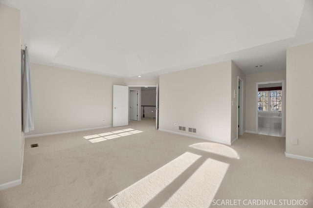 unfurnished bedroom featuring light colored carpet, a raised ceiling, and ensuite bath