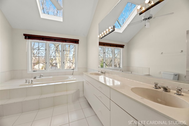 bathroom featuring toilet, lofted ceiling with skylight, vanity, a relaxing tiled tub, and tile patterned flooring