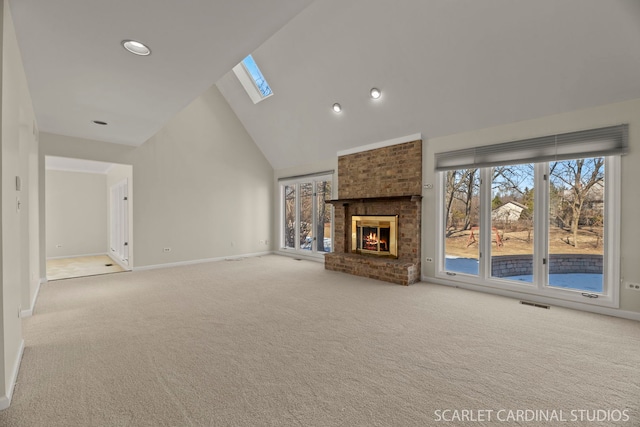 unfurnished living room featuring light colored carpet, a fireplace, a skylight, and high vaulted ceiling