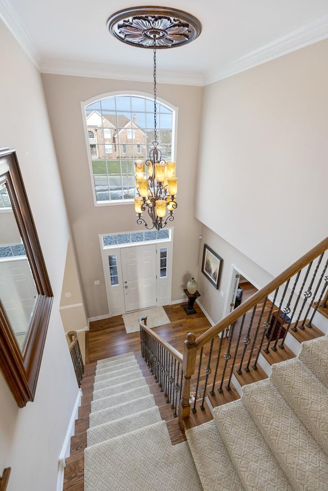 stairs with hardwood / wood-style flooring, crown molding, and a notable chandelier