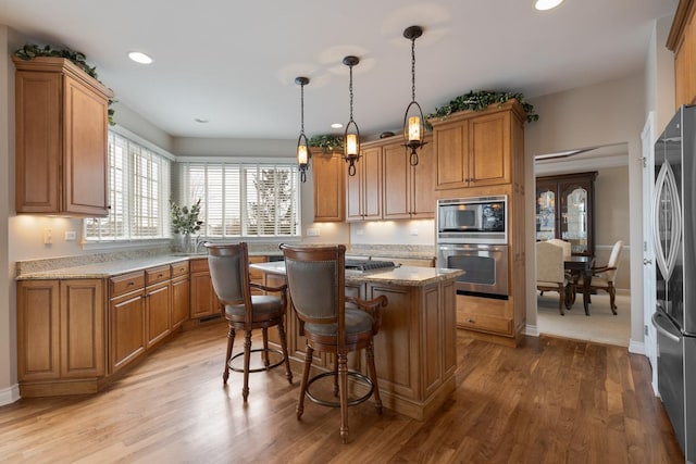 kitchen with light stone counters, appliances with stainless steel finishes, decorative light fixtures, a kitchen island, and hardwood / wood-style flooring