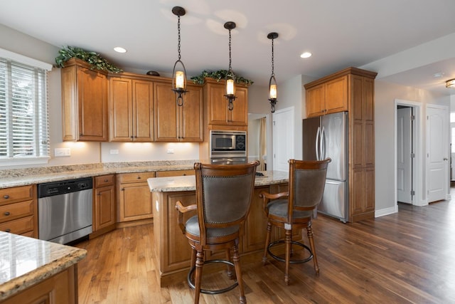 kitchen with appliances with stainless steel finishes, dark hardwood / wood-style flooring, light stone counters, pendant lighting, and a kitchen island