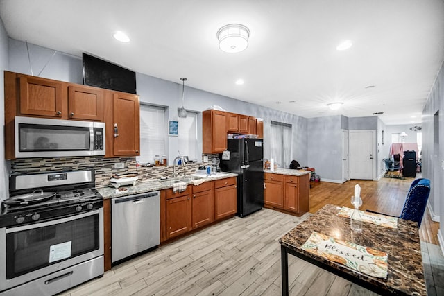 kitchen with appliances with stainless steel finishes, light hardwood / wood-style floors, light stone counters, and hanging light fixtures