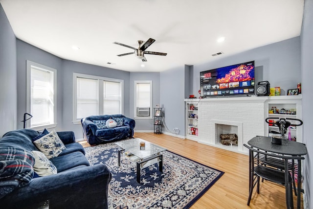 living room featuring plenty of natural light, ceiling fan, wood-type flooring, and a brick fireplace