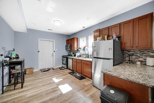 kitchen featuring backsplash, light stone countertops, stainless steel appliances, and light wood-type flooring