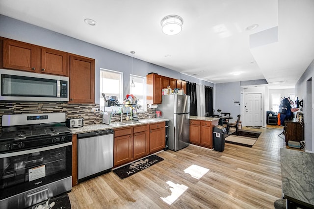 kitchen with light stone countertops, decorative backsplash, light wood-type flooring, and appliances with stainless steel finishes