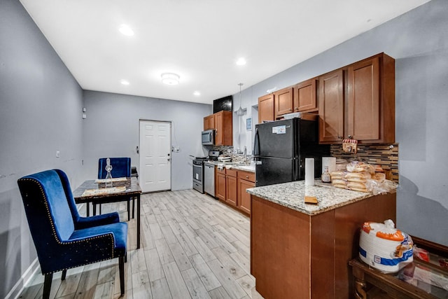 kitchen with light stone countertops, stainless steel appliances, kitchen peninsula, decorative backsplash, and light wood-type flooring