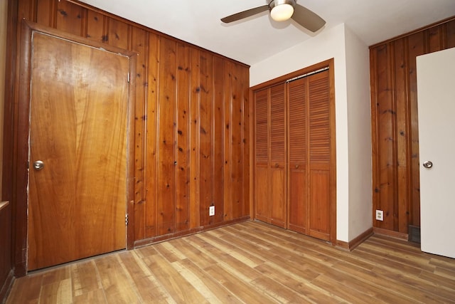 unfurnished bedroom featuring light wood-type flooring, a closet, ceiling fan, and wood walls