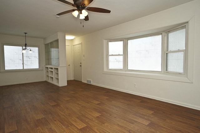 empty room with ceiling fan with notable chandelier and dark wood-type flooring