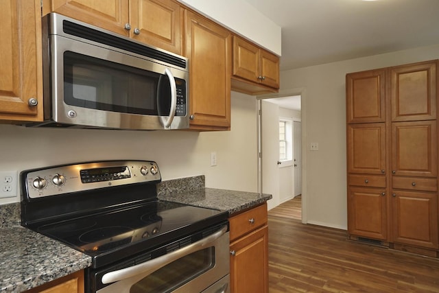 kitchen with dark hardwood / wood-style flooring, stainless steel appliances, and dark stone counters