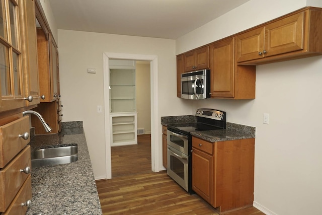 kitchen featuring appliances with stainless steel finishes, dark stone counters, dark wood-type flooring, and sink