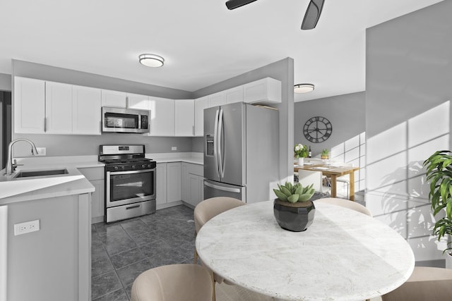 kitchen featuring ceiling fan, sink, stainless steel appliances, white cabinets, and dark tile patterned flooring