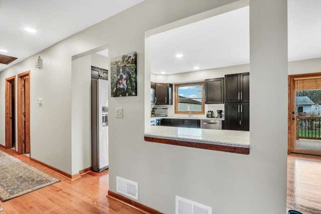 kitchen featuring light stone countertops, kitchen peninsula, light wood-type flooring, dark brown cabinetry, and stainless steel appliances