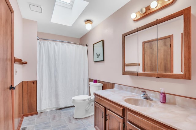 bathroom with vanity, wood walls, toilet, and a skylight