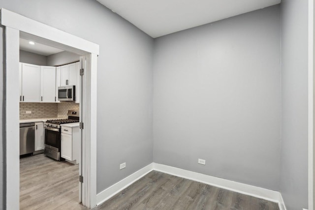 kitchen with backsplash, stainless steel appliances, white cabinetry, and light hardwood / wood-style floors