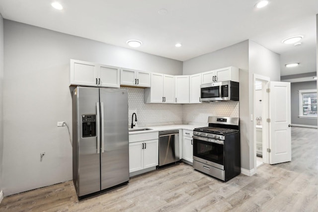 kitchen with decorative backsplash, light wood-type flooring, stainless steel appliances, sink, and white cabinets