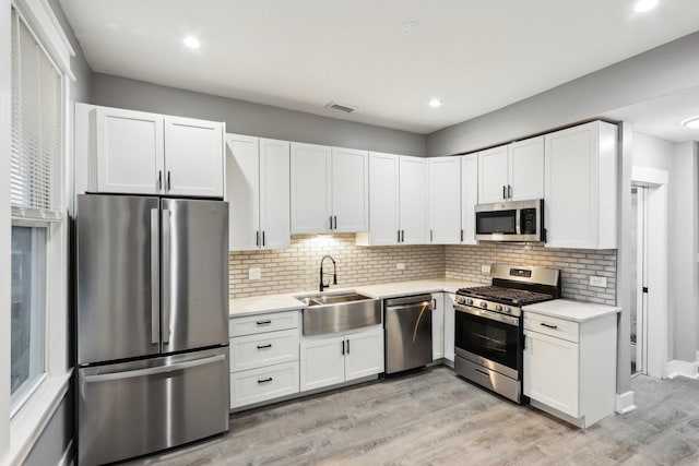 kitchen featuring sink, stainless steel appliances, backsplash, white cabinets, and light wood-type flooring