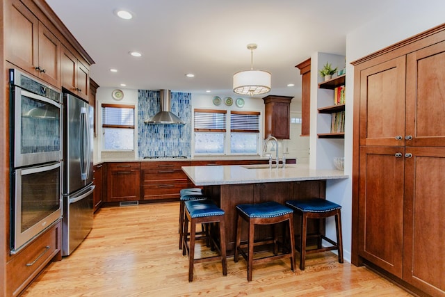 kitchen with light stone counters, stainless steel appliances, wall chimney range hood, a kitchen bar, and sink