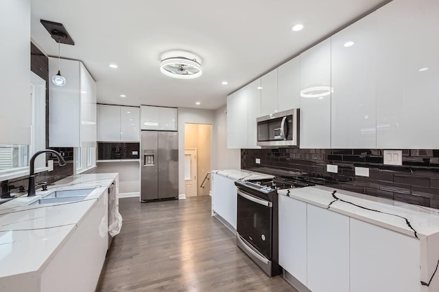 kitchen with appliances with stainless steel finishes, dark hardwood / wood-style flooring, sink, white cabinetry, and hanging light fixtures