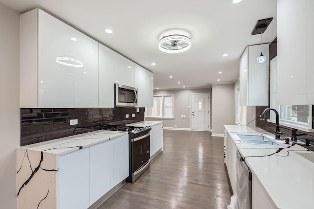 kitchen featuring appliances with stainless steel finishes, sink, white cabinets, dark hardwood / wood-style floors, and hanging light fixtures