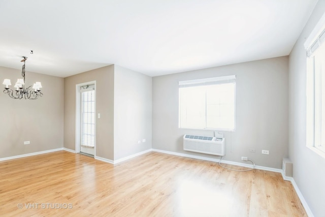 empty room with a notable chandelier, a wall unit AC, and light hardwood / wood-style flooring