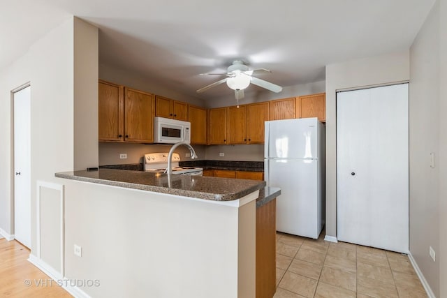 kitchen with kitchen peninsula, white appliances, ceiling fan, and dark stone countertops