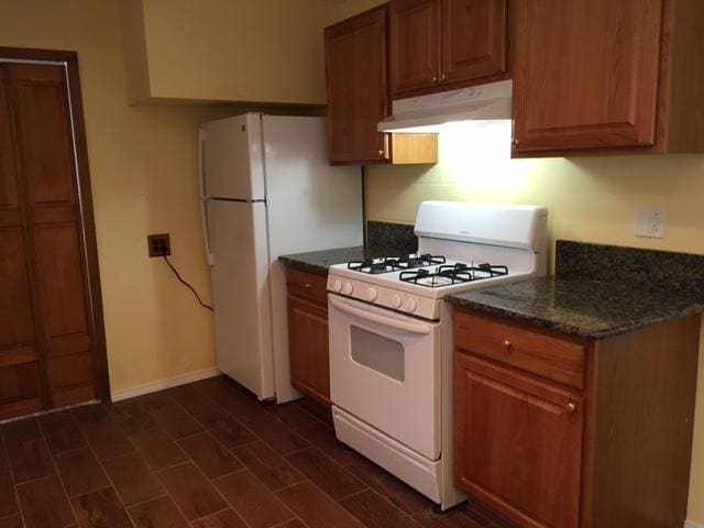 kitchen featuring dark stone counters and white appliances