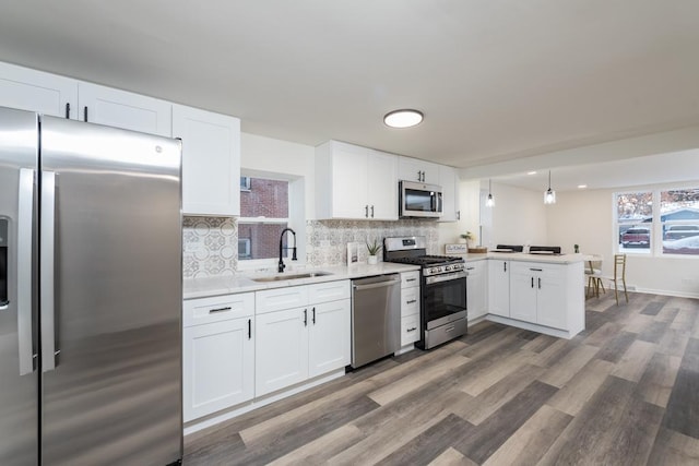 kitchen featuring kitchen peninsula, appliances with stainless steel finishes, sink, decorative light fixtures, and white cabinets