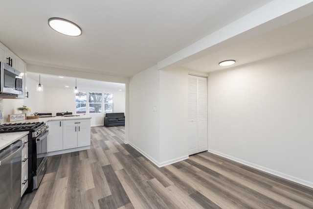 kitchen with kitchen peninsula, appliances with stainless steel finishes, decorative light fixtures, dark hardwood / wood-style flooring, and white cabinetry