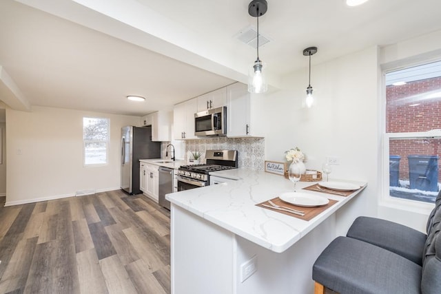 kitchen with kitchen peninsula, appliances with stainless steel finishes, white cabinets, hardwood / wood-style floors, and hanging light fixtures