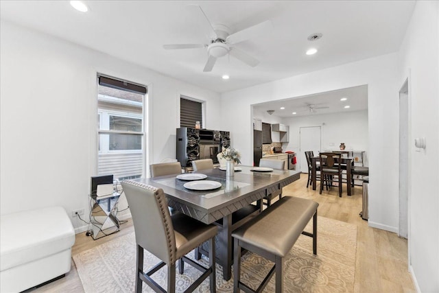 dining room featuring a fireplace, light wood-type flooring, and ceiling fan