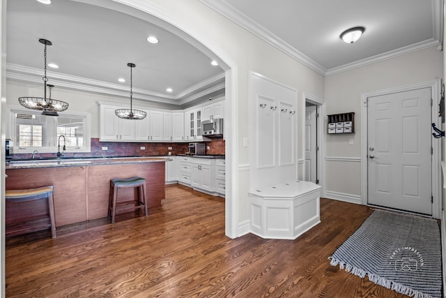 kitchen with glass insert cabinets, stainless steel microwave, ornamental molding, hanging light fixtures, and white cabinetry