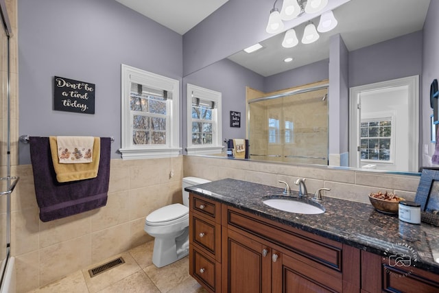 bathroom featuring tile walls, visible vents, toilet, a shower stall, and vanity