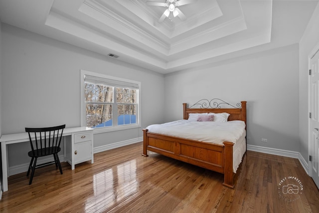 bedroom featuring baseboards, a raised ceiling, visible vents, and light wood-style floors