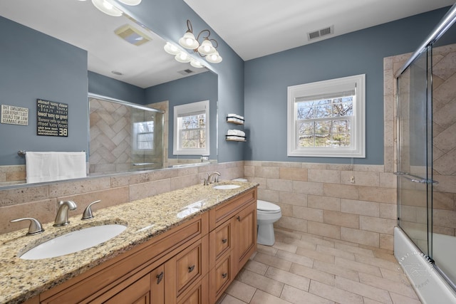 full bath with toilet, a sink, visible vents, and tile walls