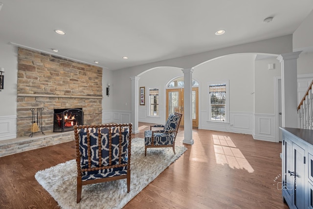 living room featuring decorative columns, a stone fireplace, a decorative wall, and wood finished floors