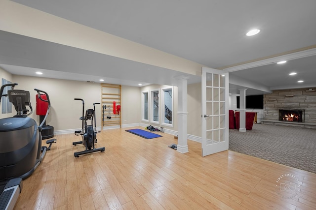 workout area featuring light wood-type flooring, a stone fireplace, baseboards, and recessed lighting