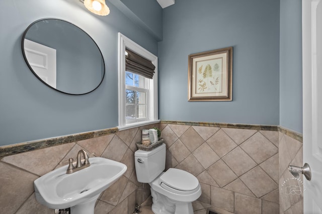 half bath featuring toilet, a wainscoted wall, tile walls, and a sink