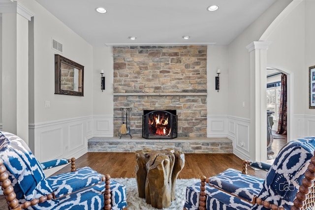 living area featuring dark wood-style floors, decorative columns, visible vents, and a stone fireplace